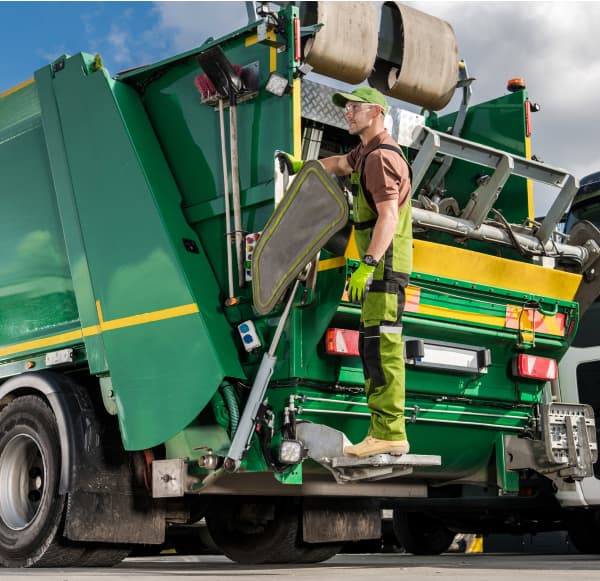 Worker in green overalls beside open, brightly colored trash truck ready for waste collection