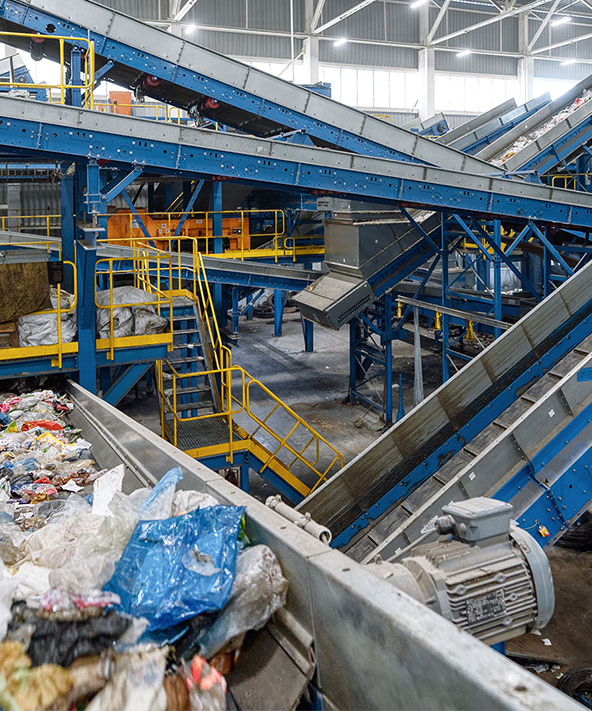Recycling facility with blue conveyors and machines processing waste, surrounded by safety railings