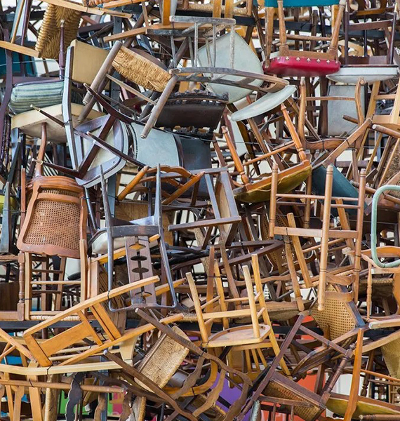 A messy stack of old wooden and metal chairs in various styles, colors, and shapes.