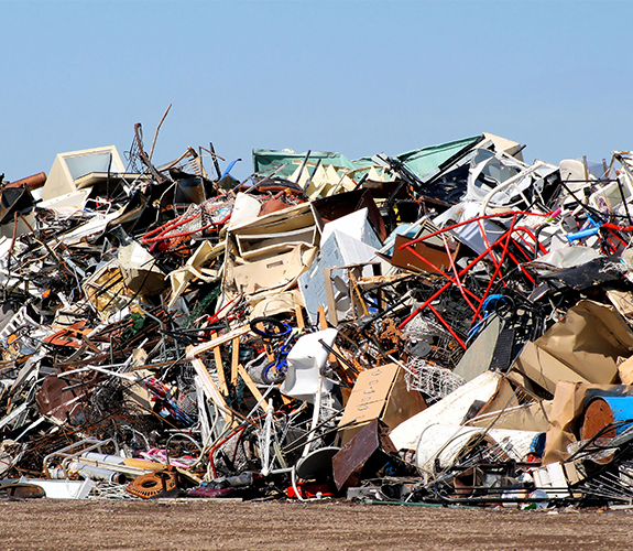 A large pile of scrap metal, junk, bikes, and furniture under a clear blue sky.